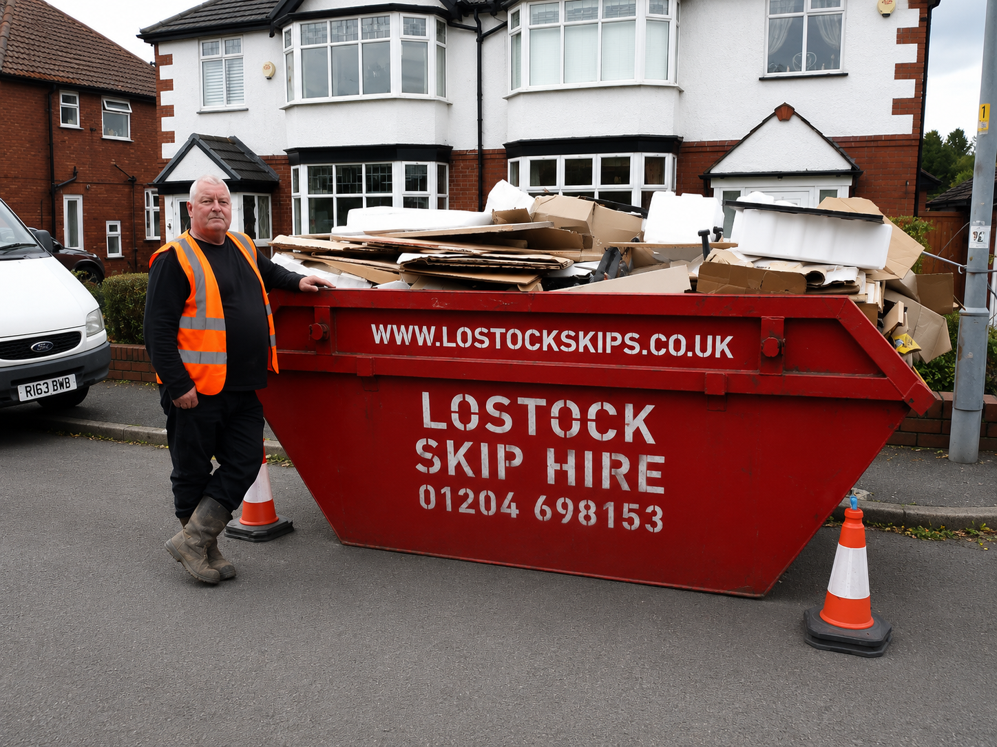 Worker in orange hi-vis vest beside a red skip filled with cardboard on a residential street